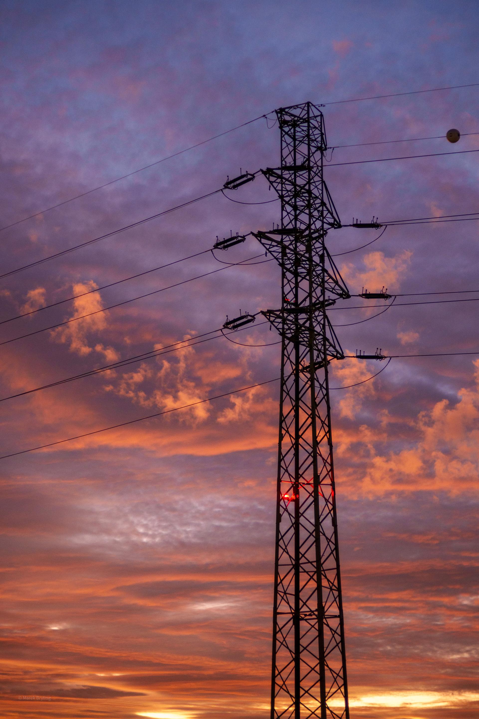 Słup wysokiego napięcia na tle malowniczego, pomarańczowo-fioletowego zachodu słońca.
