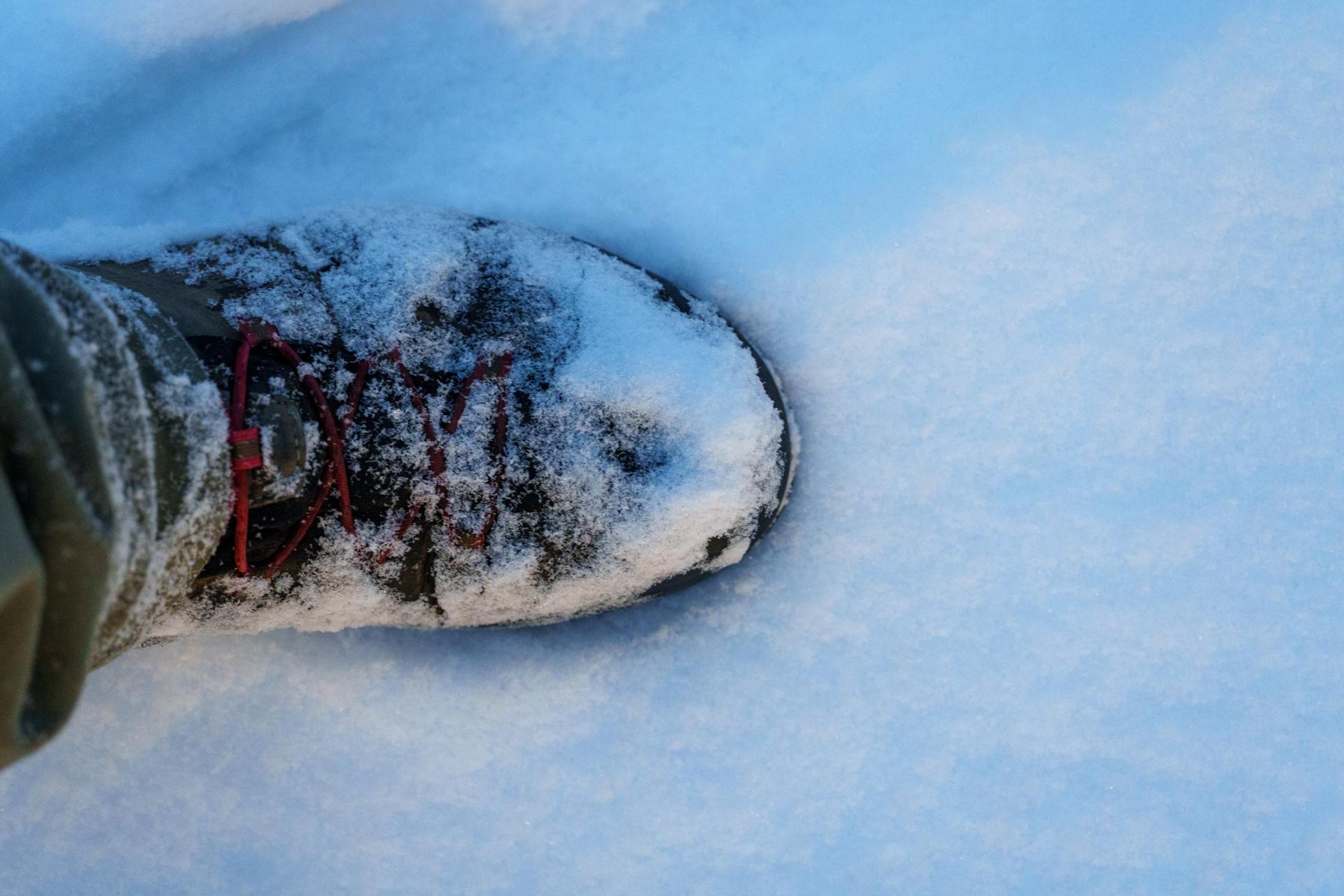 Widok z góry na buta pokrytego śniegiem podczas zimowej wędrówki. Mroźna sceneria i biały puch pod nogami.